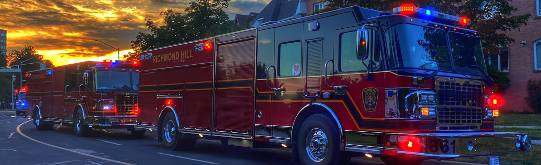 two firetrucks are parked on a street at sunset